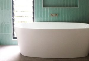 shows beautiful big bath bathed in light with long thin tourquoise feature tiles