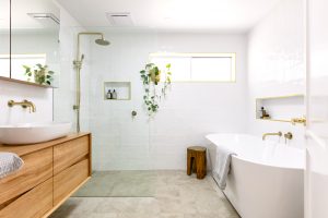 image shows a light filled bathroom with timber vanity and brushed gold tapware